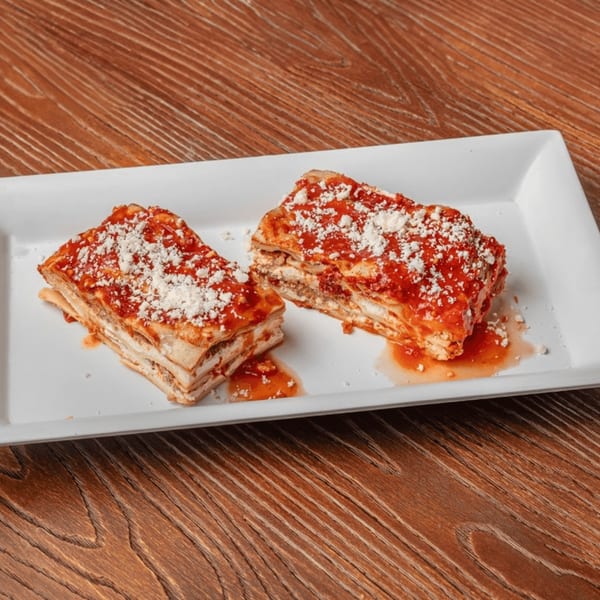 Two slices of Nonna's Italian Deli & Market lasagna with red sauce and grated cheese on a white plate.