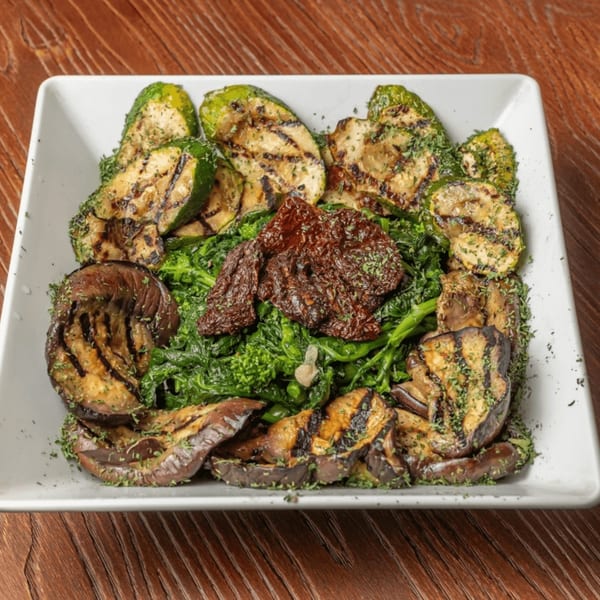 Grilled zucchini and eggplant slices with broccoli rabe and sun-dried tomatoes on a white plate.