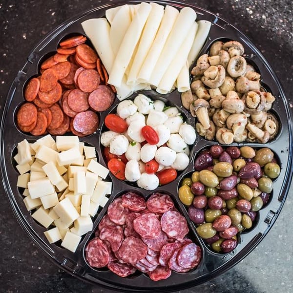 A black platter with compartments filled with Italian meats, cheeses, olives, mushrooms, and mozzarella.