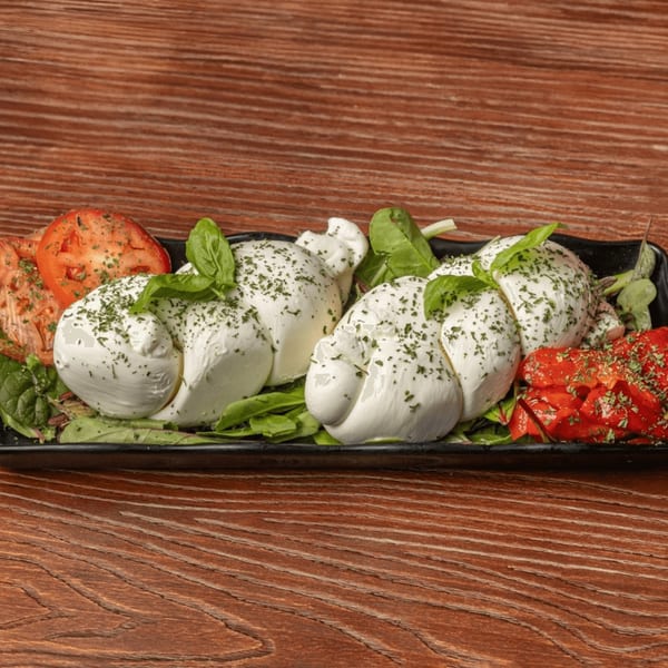 Fresh mozzarella balls with basil, tomatoes, and greens on a black platter.